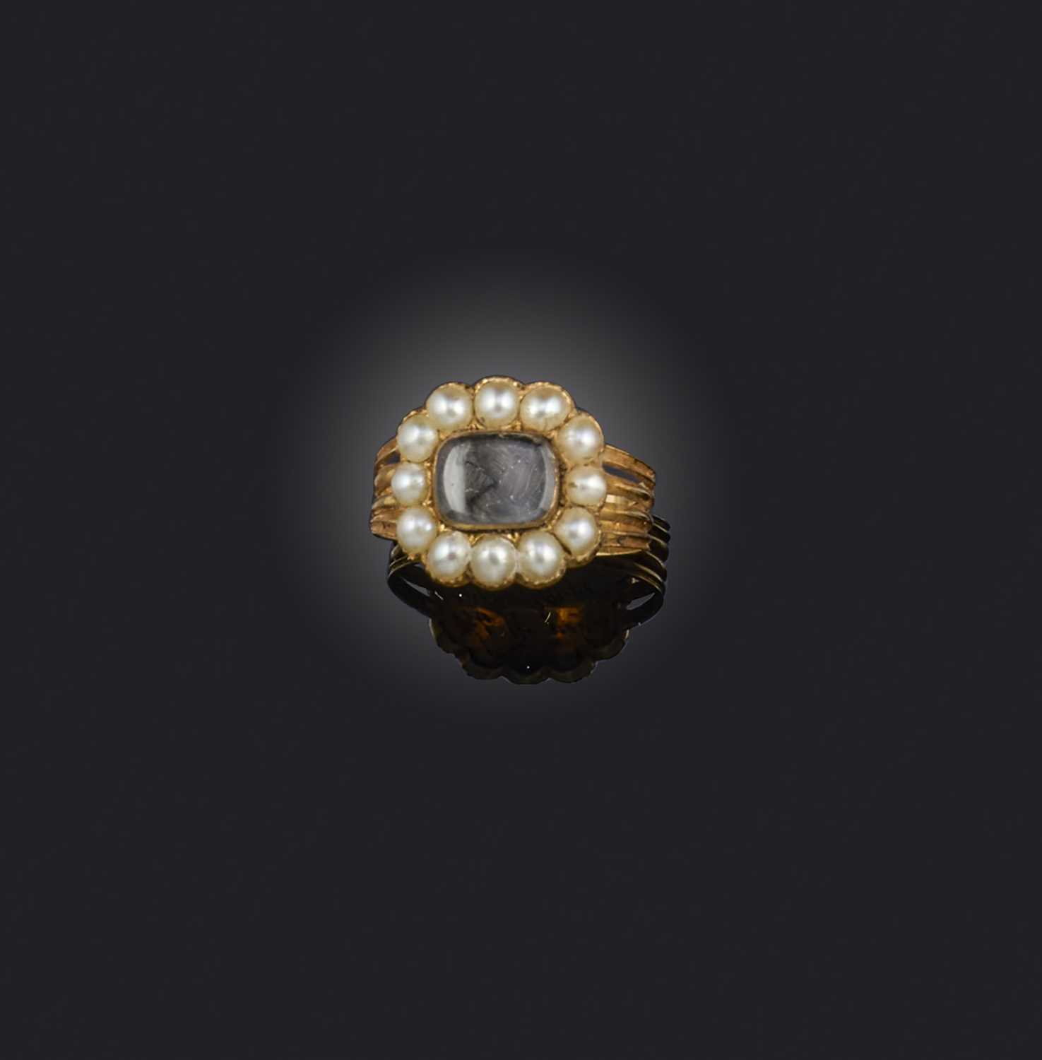 An early 19th century seed pearl mourning ring, centring on a glazed locket compartment within a