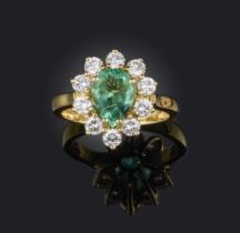 An emerald and diamond ring, of cluster design, claw-set with a pear-shaped emerald weighing