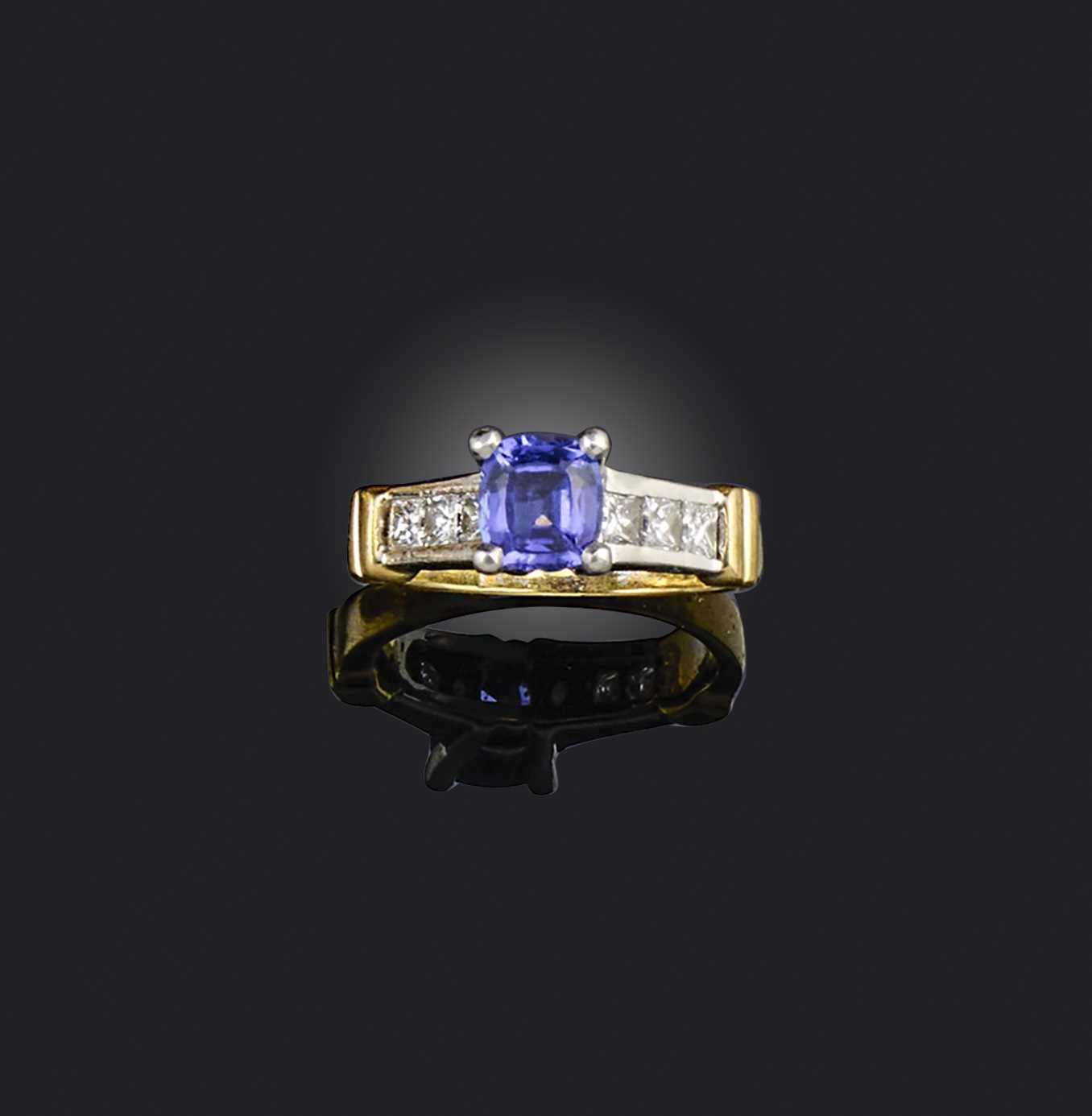 A tanzanite and diamond ring, claw-set with a cushion-shaped tanzanite, to shoulders channel-set