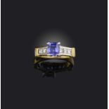 A tanzanite and diamond ring, claw-set with a cushion-shaped tanzanite, to shoulders channel-set