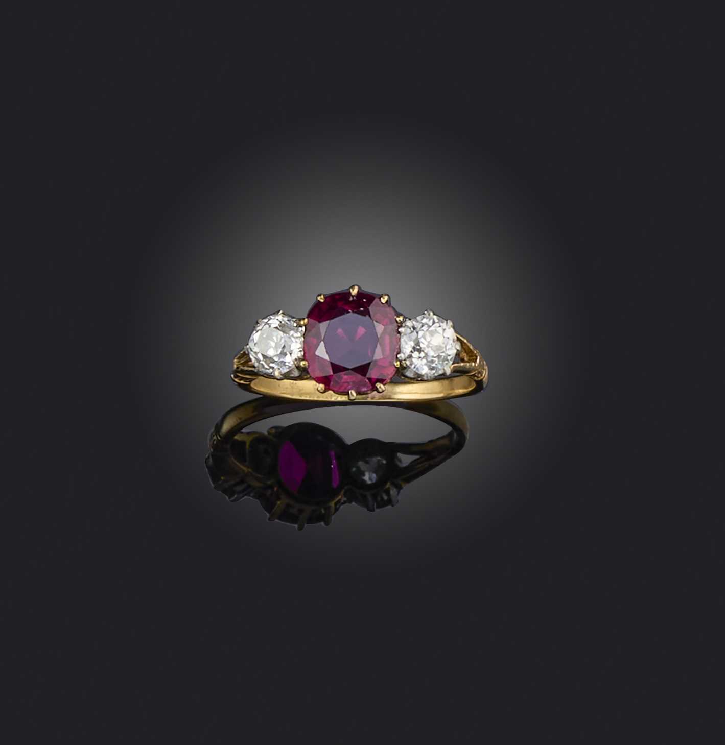 A ruby and diamond three-stone ring, late 19th century, the cushion-shaped ruby flanked by a pair of