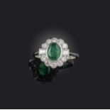An emerald and diamond cluster ring, the oval-shaped emerald weighing 1.10cts, within a diamond-