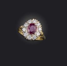 A ruby and diamond ring, of cluster design, set with an oval ruby measuring approximately 7.7 x 6.