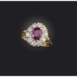 A ruby and diamond ring, of cluster design, set with an oval ruby measuring approximately 7.7 x 6.