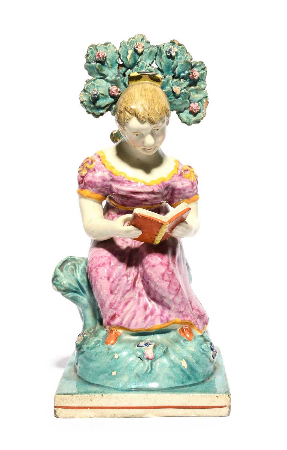 A Staffordshire figure of a girl, 1st half 19th century, seated on a rocky stump beneath flowering