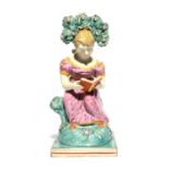 A Staffordshire figure of a girl, 1st half 19th century, seated on a rocky stump beneath flowering