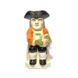 An unusual Pratt ware Toby jug, c.1800, seated with a patterned jug of ale, wearing an ochre coat