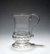 A glass mug, c.1780, of bell shape, the base moulded with a band of gadroons, the strap handle