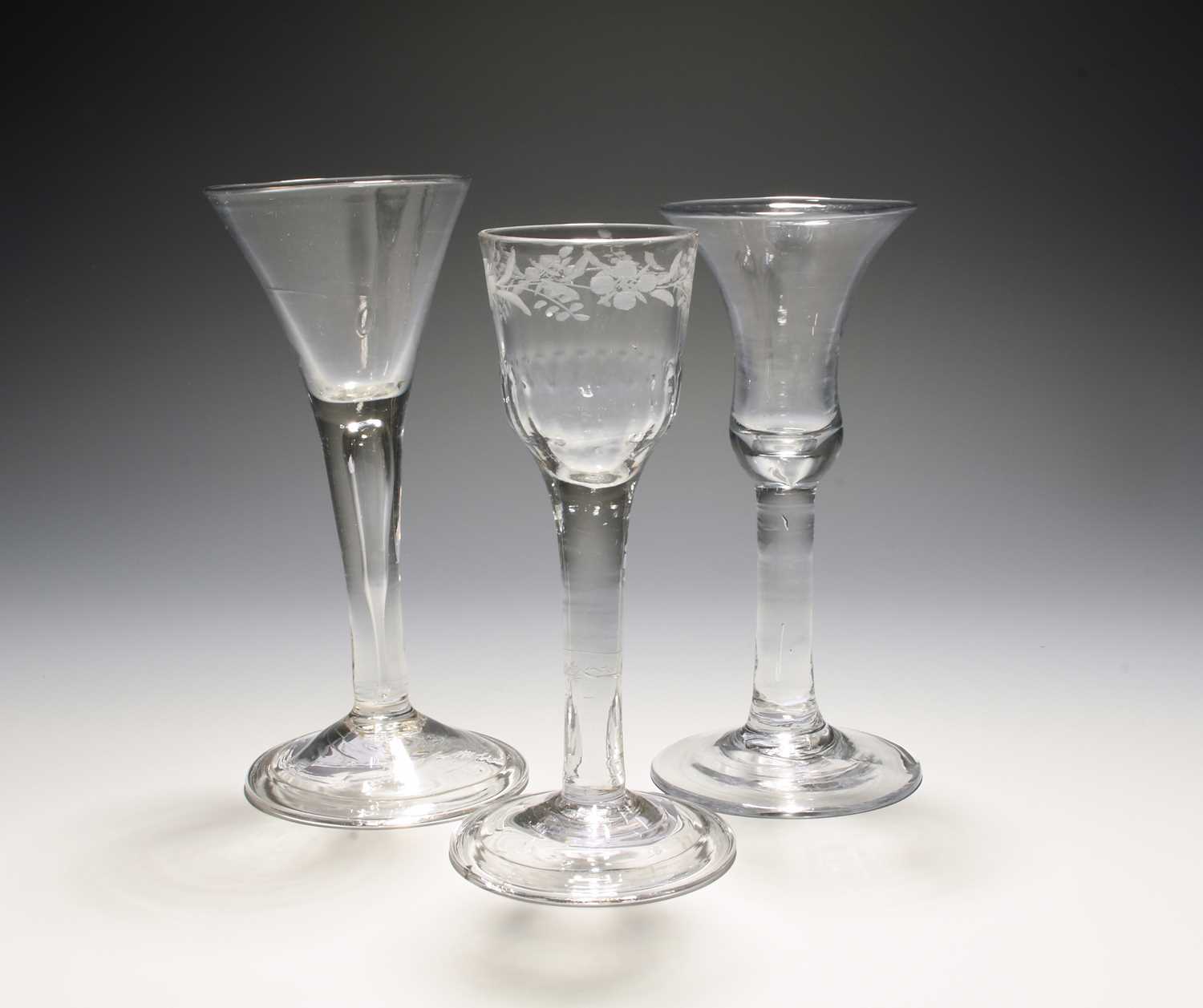 Three wine glasses, mid 18th century, one with a bell bowl on a plain stem, another a drawn