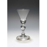 A baluster wine glass, c.1720, the bell bowl with a solid base enclosing a single tear, raised on