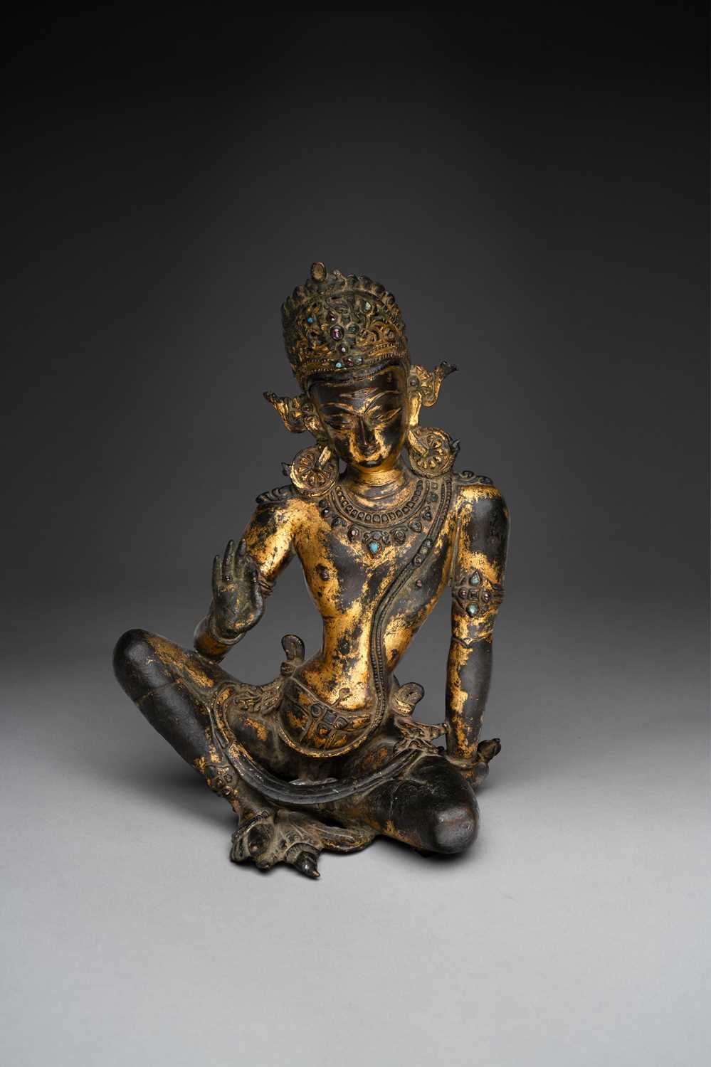 A RARE NEPALESE GILT-COPPER FIGURE OF INDRA 14TH CENTURY Seated in maharajalilasana with his right