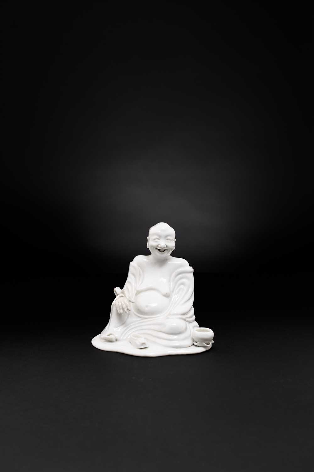 A CHINESE WHITE-GLAZED FIGURE OF A SEATED LUOHAN 18TH CENTURY Modelled wearing loose monk’s robes,