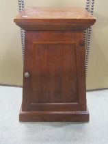 A small stained hardwood pedestal side cupboard, of tapered form, the stepped top above a panelled