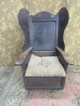 An 18th century oak lambing chair with fielded panel back and deep winged sides, the shaped arms