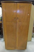 An Ercol medium elm wardrobe enclosed by a pair of full length rectangular panelled doors and raised