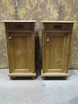 A pair of stripped and waxed pine bedside cabinets each enclosed by a panelled door and frieze