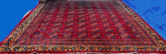 A large Turkoman type carpet with ten rows of multi coloured medallions on a red ground, with a