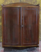 An Edwardian mahogany hanging wall cupboard with serpentine front enclosed by a pair of