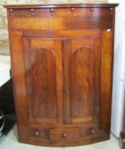 A 19th century mahogany bowfronted corner cupboard enclosed by a pair of arched panelled doors
