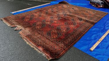An Antique Afghan wool carpet with three rows of interlocking medallions on a rusty faded red