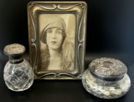 A silver metal photo frame and two silver lidded glass dressing table pots (3)