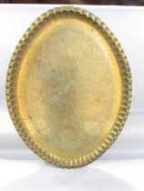 An oval Middle Eastern richly engraved brass tray, 87cm x 65cm, with a wooden stand