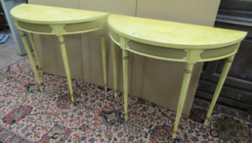 A pair of demi-lune tables raised on four turned supports with overall painted finish