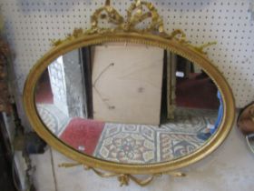 An oval gilt framed wall mirror with beaded slip and tied ribbon surmount, 77 x 78cm
