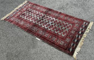 A Bokhara carpet with a central panel of red gul on a green ground 200cm x 100cm.