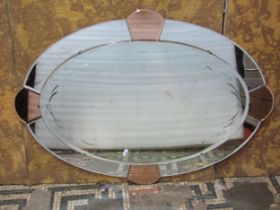 An Art Deco wall mirror of oval form, the mirrored frame with peach coloured panels, 65cm x 90cm
