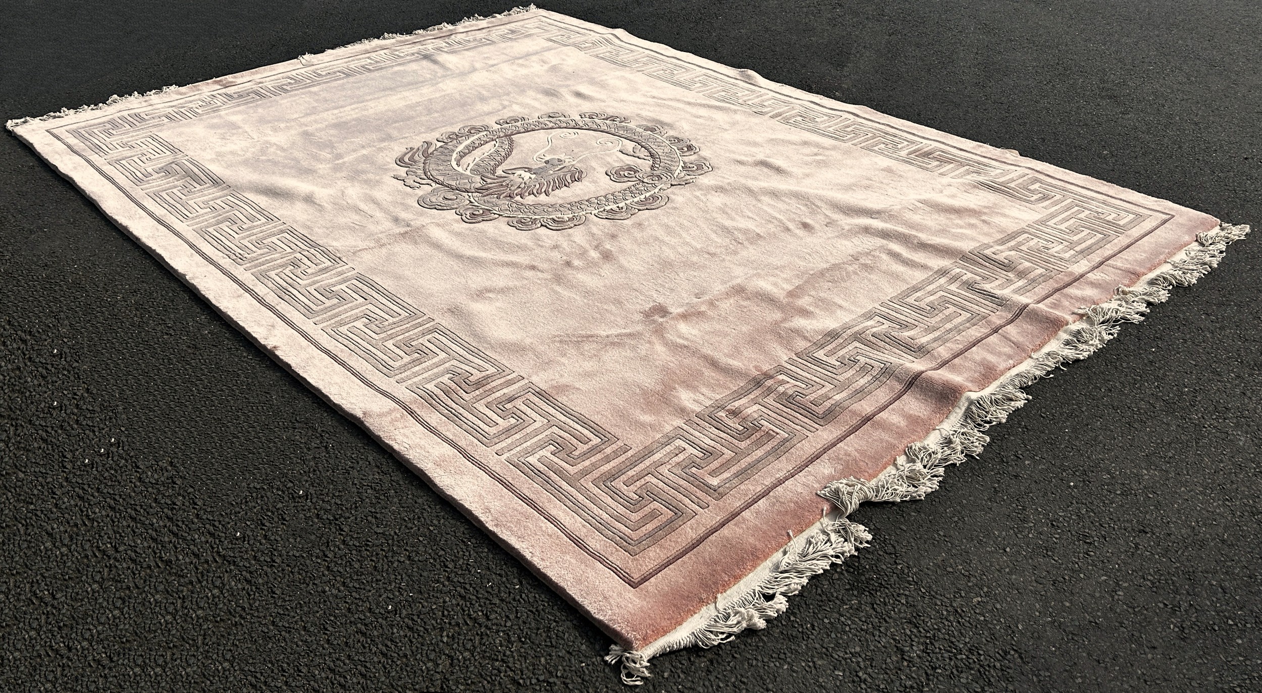 A large Chinese pink thick wool pile carpet with a coiled dragon to the centre and a geometric