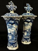 A pair of hand painted continental tin glazed trumpet shaped vases and covers, decorated with scenes