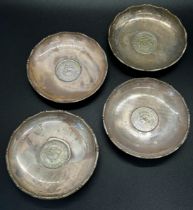 A collection of seven silver dishes with coins inserted depicting different heads of state, together