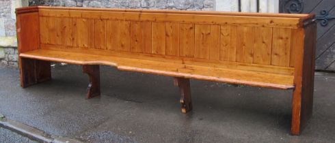 A pine church pew with shaped planked seat and boarded back beneath moulded rail, one end with