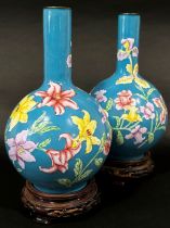 A pair of Chinese enamelled vases of bulbous form with drawn necks and foliate detail, raised on