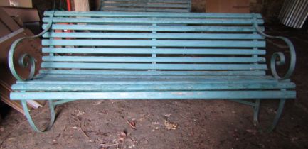 An old garden bench with green painted wooden slatted seat and back raised on sprung steel supports,