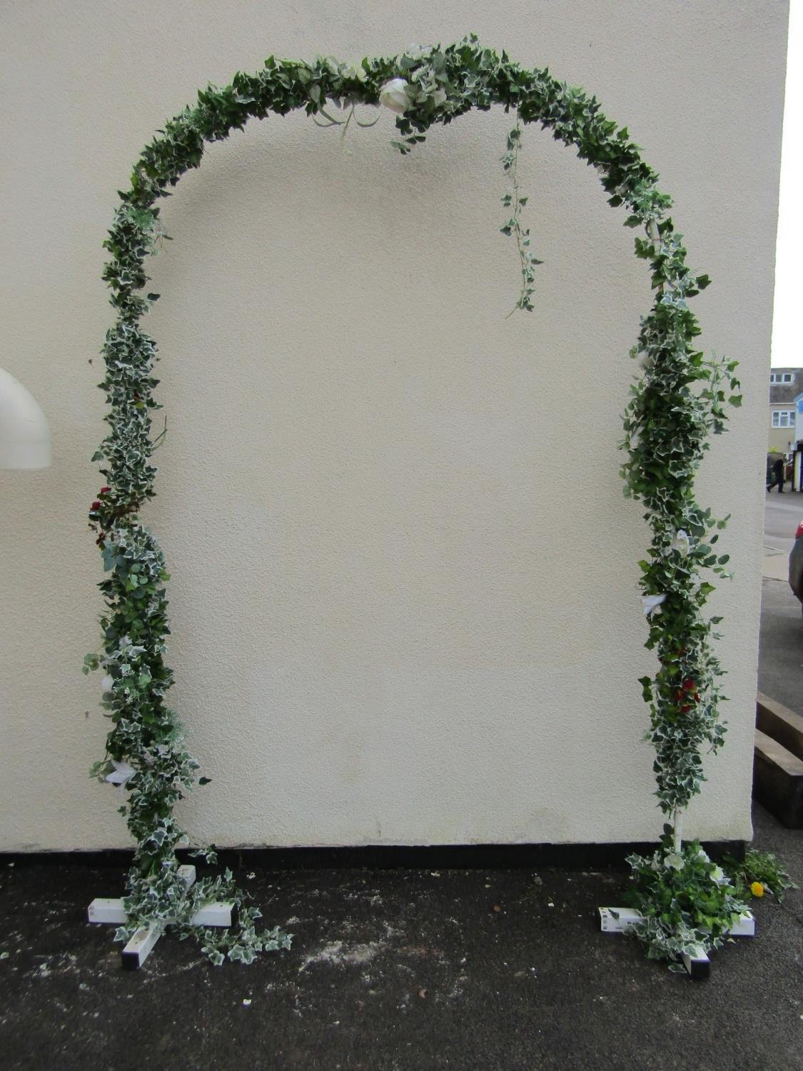 A painted square tubular steel framed wedding arch with trailing artificial ivy and floral detail,