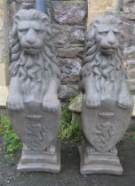 A pair of cast composition stone pier/garden ornaments in the form of seated lions clutching