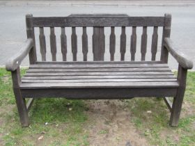 A heavy gauge weathered teak garden bench with slatted seat and back with chamfered detail beneath a