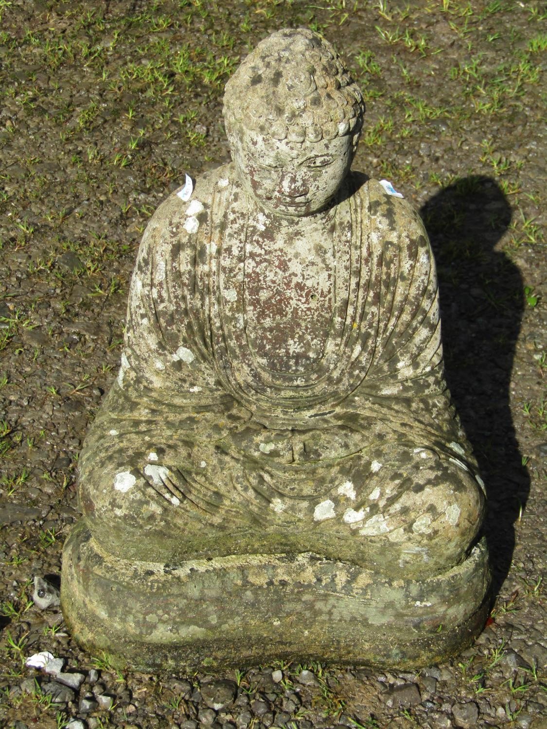 A cast composition stone garden ornament in the form of a seated Buddha in lotus position, raised on