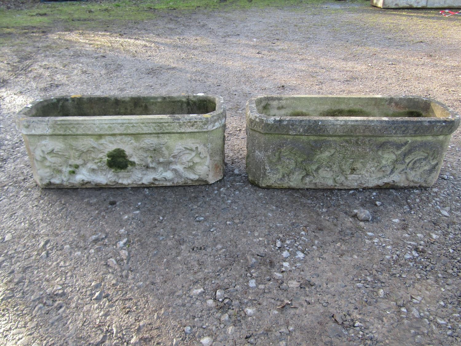A pair of weathered rectangular cast composition stone flower troughs with canted corners, lions