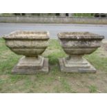 A pair of weathered cast composition stone garden urns of squat square cut and tapered form with