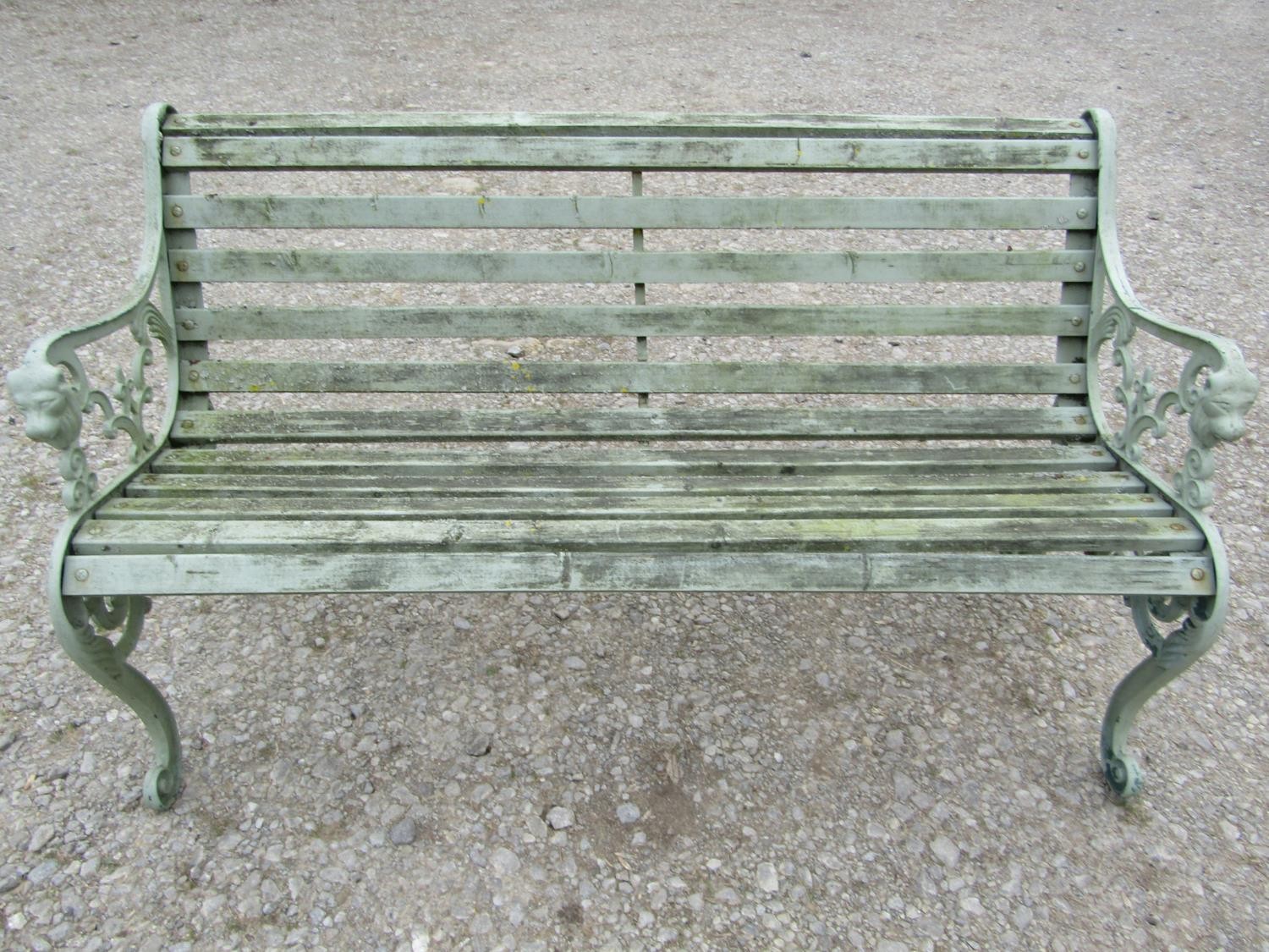 A light green painted garden bench with wooden slatted seat raised on decorative pierced and