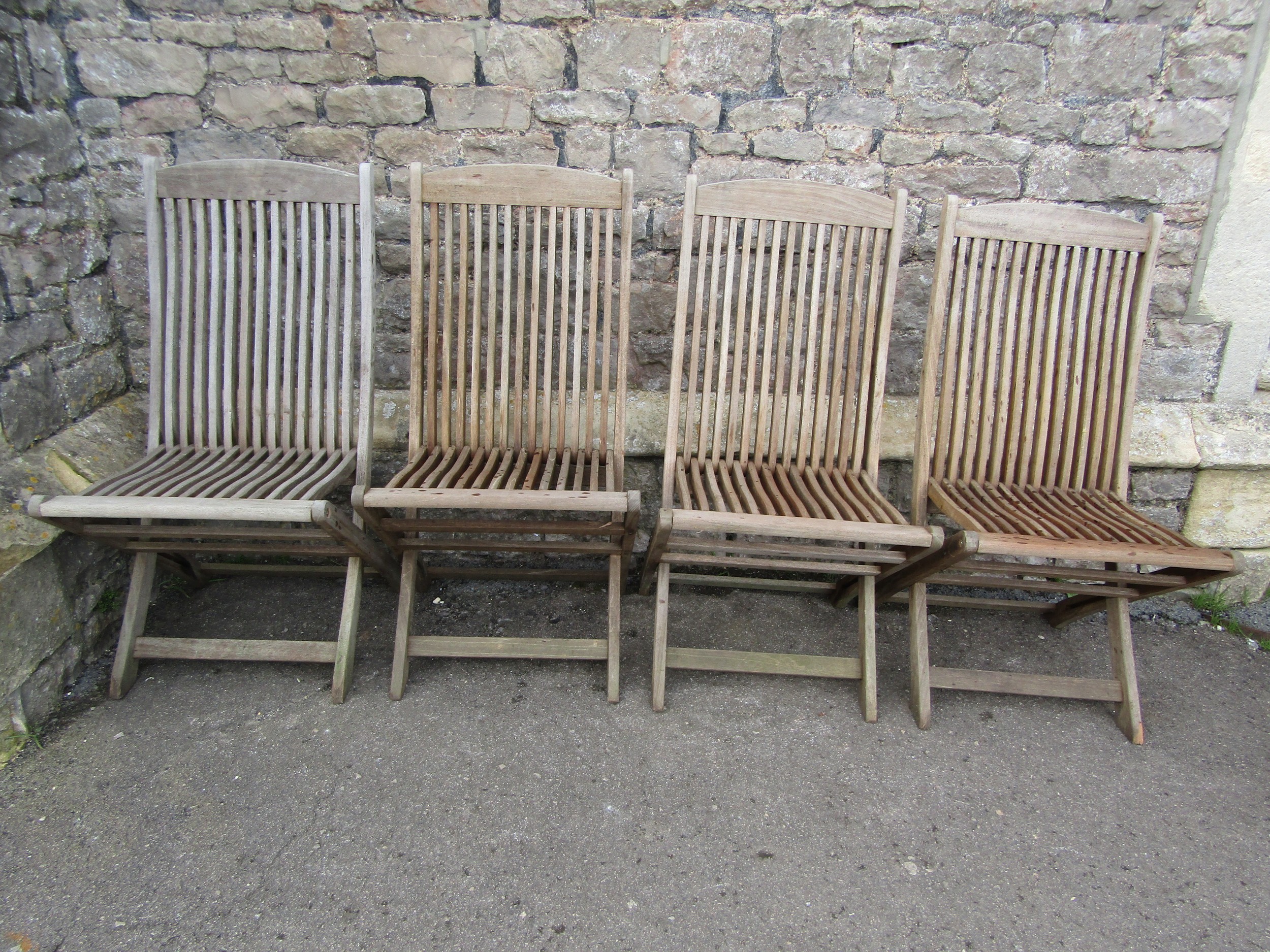 A set of four weathered Windsor Set folding teak garden chairs with slatted seats and backs