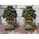 A pair of weathered two sectional cast composition stone garden ornaments in the form of fruiting