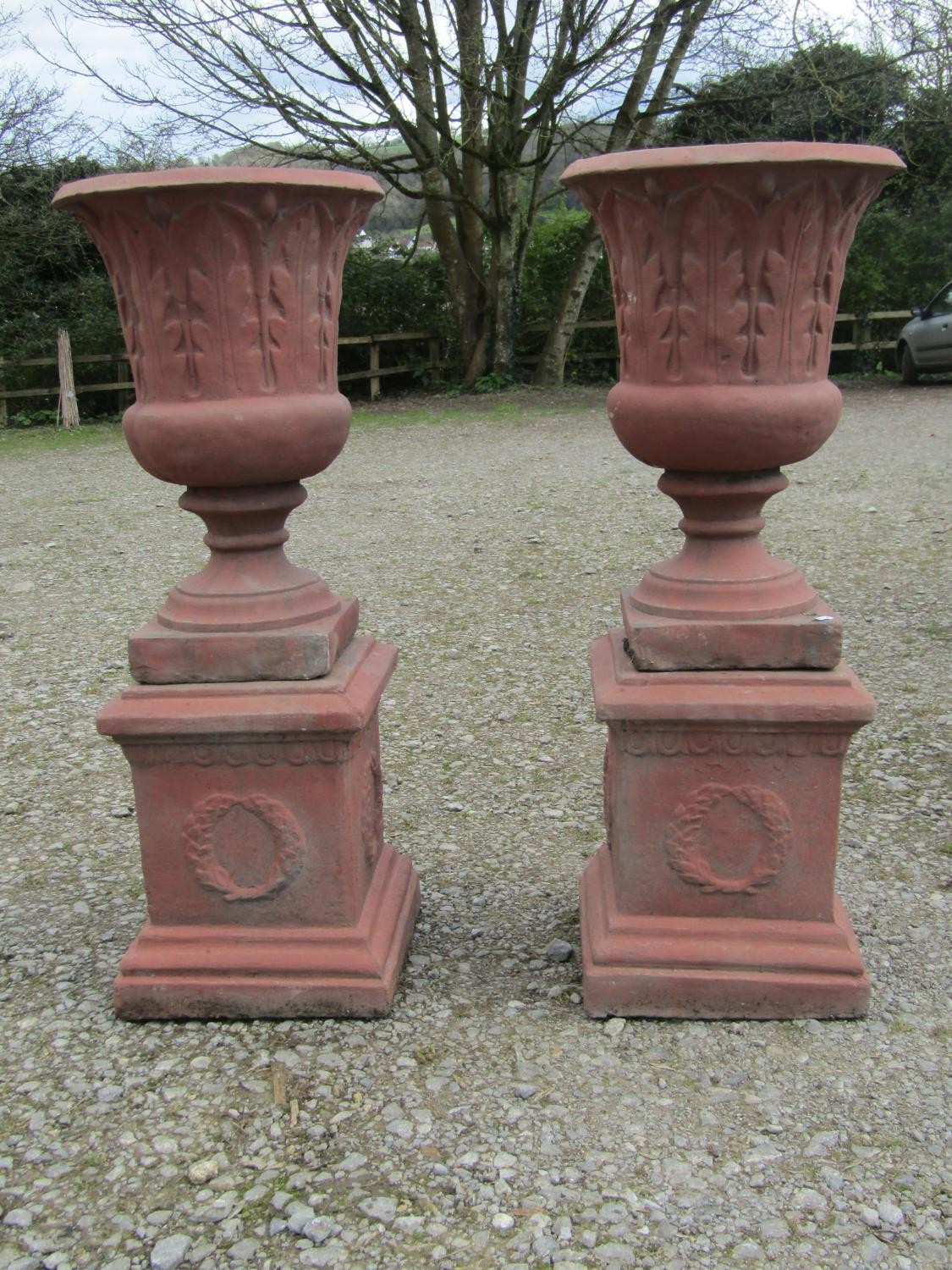 A pair of faux terracotta cast composition stone trumpet shaped garden urns with repeating leaf