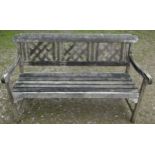 A weathered three seat garden bench with slatted seat and lattice panelled back beneath a shaped