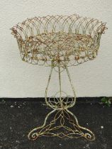 A weathered wire work jardinière with lattice detail and scrolled supports, 53 cm diameter x 82 cm
