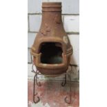 A weathered clay two sectional chimenea with moth and butterfly relief detail and raised on a