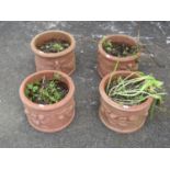 A matched set of four weathered squat cylindrical terracotta planters with repeating raised relief